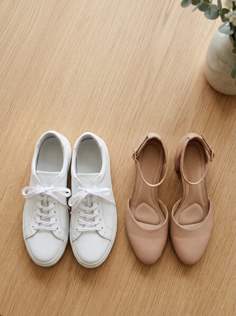 White sneakers next to a pair of nude heels beside the hem of a neutral dress
